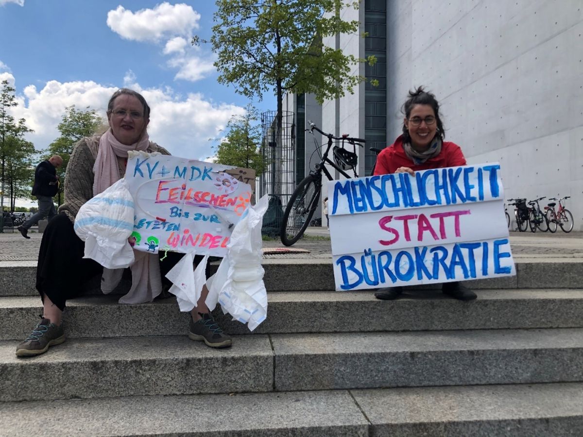 2 Frauen sitzen mit Demoplakaten auf Stufen.