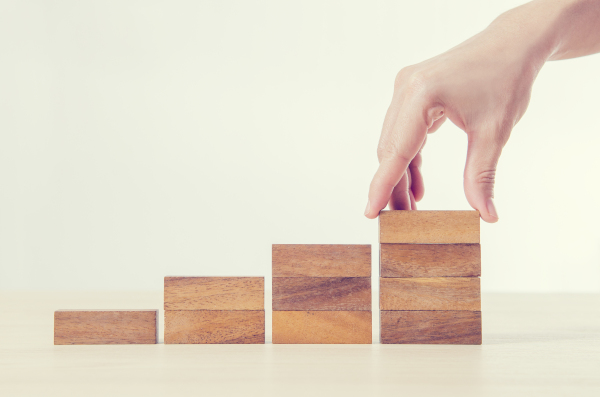 Vier Bausteine, wie eine Treppe aufgebaut, werden von einer Hand hingestellt.